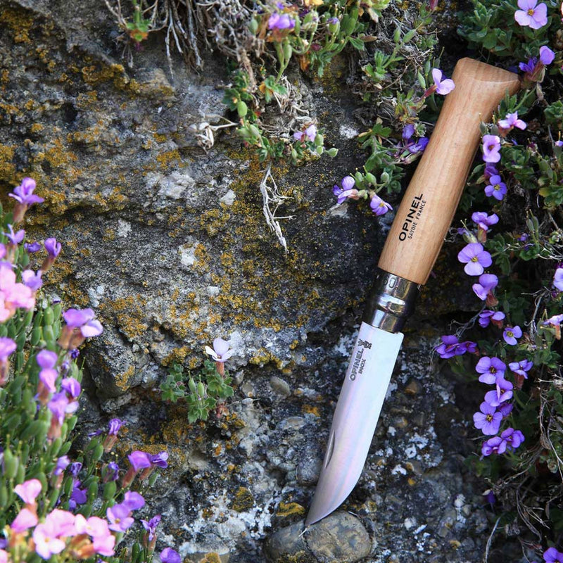 Couteau Opinel no 9 posé sur un rocher fleuri en montagne